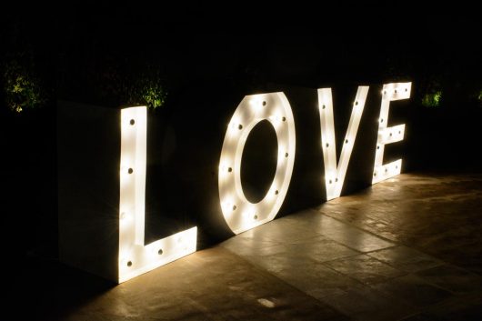 Φωτεινά γράμματα σχηματίζουν τη λέξη LOVE και είναι ένα τραπέζι για το βιβλίο ευχών ή το candy bar που προτείνουμε στα ζευγάρια
